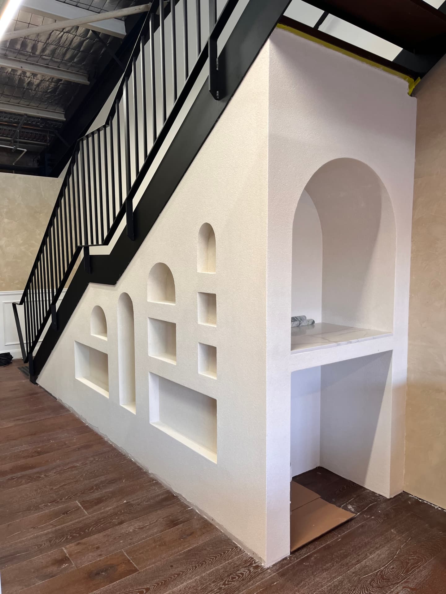 Feature plaster wall under a staircase with arched and square recessed niches